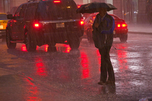 a man with umbrella crosses a street at night in the rain